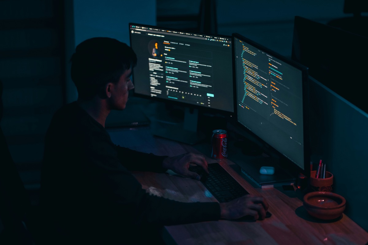 Young developer at a dual-monitor setup with code on screen, blue-toned night scene